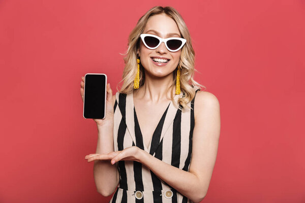 Красивая удивительная молодая женщина позирует изолированные на красном коралловом фоне, показывая дисплей мобильного телефона
.