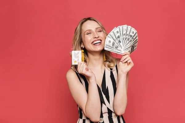 Hermosa mujer joven increíble posando aislada sobre fondo de coral rojo con tarjeta de crédito y dinero . — Foto de Stock