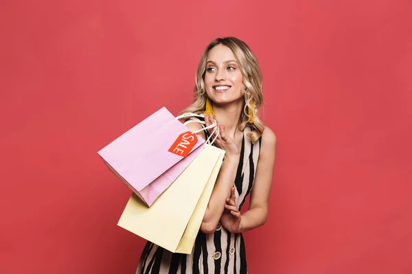 Amazing young woman posing isolated over red coral background holding shopping bags. — Stock Photo, Image