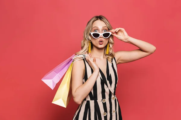 Fantastisk ung kvinna poserar isolerade över röda korall bakgrund hålla shoppingväskor. — Stockfoto