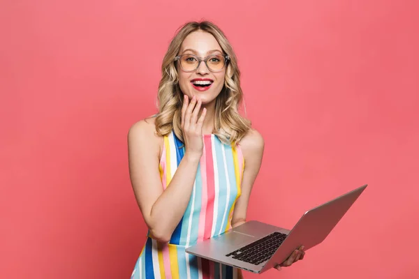 Mujer joven emocionada posando aislada sobre fondo de coral rojo usando computadora portátil . — Foto de Stock