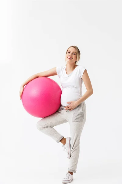 Mooie jonge zwangere yoga fitness vrouw poseren geïsoleerd over witte muur achtergrond maken oefeningen met bal. — Stockfoto