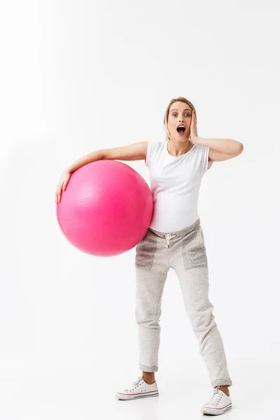 Όμορφη σοκαρισμένος νέος έγκυος γιόγκα Fitness γυναίκα που παρουσιάζουν απομονωμένα πάνω λευκό τοίχο φόντο κάνει ασκήσεις με μπάλα. — Φωτογραφία Αρχείου