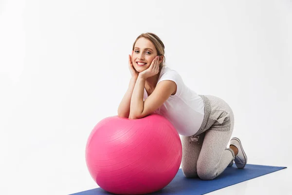 Mooie jonge zwangere yoga fitness vrouw poseren geïsoleerd over witte muur achtergrond maken oefeningen met bal. — Stockfoto