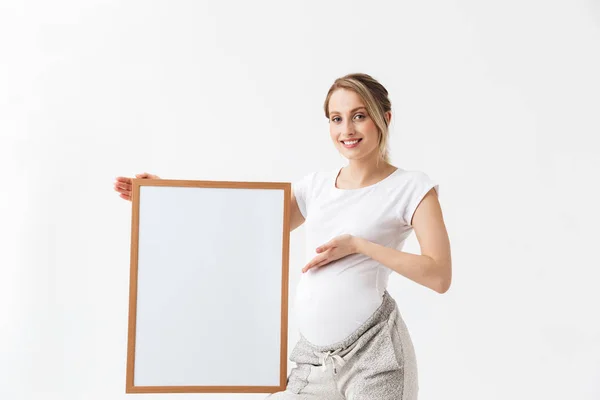 Όμορφη νεαρή έγκυο γυναίκα που θέτει απομονωμένα πάνω από λευκό τοίχο φόντο κρατώντας χώρο αντιγραφής κενό. — Φωτογραφία Αρχείου