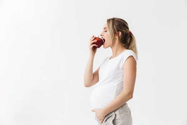 Красива молода вагітна жінка позує ізольовано на білому тлі стіни, тримаючи яблуко їсти здорову їжу . — стокове фото