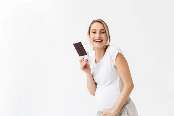 Szép fiatal terhes nő pózol elszigetelt fehér fal háttérben tartó csokoládé. — Stock Fotó