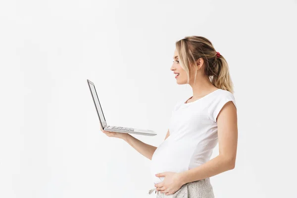 Boldog fiatal terhes nő pózol elszigetelt fehér fal háttér használ laptop számítógép. — Stock Fotó