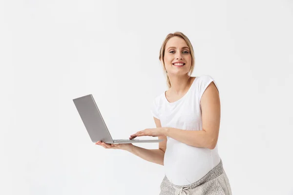 Szczęśliwa młoda kobieta w ciąży pozowanie na białym tle ściany za pomocą komputera przenośnego. — Zdjęcie stockowe
