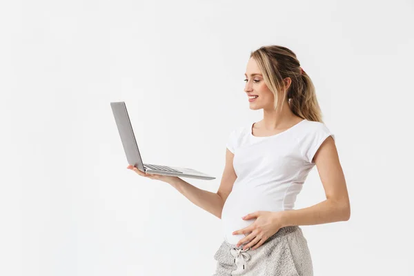 Feliz jovem grávida posando isolado sobre fundo da parede branca usando computador portátil . — Fotografia de Stock
