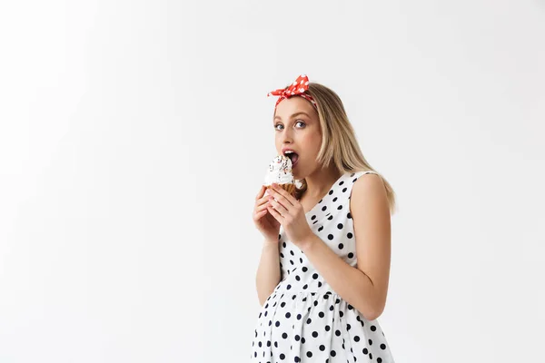 Emotivo giovane donna incinta posa isolato su sfondo muro bianco mangiare cupcake . — Foto Stock