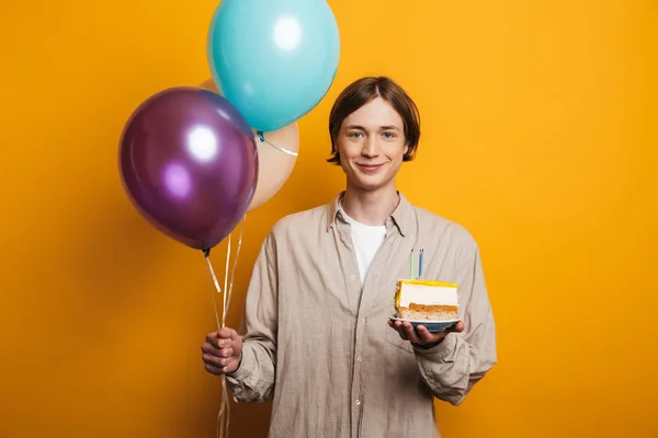 Uśmiechnięty przystojny mężczyzna w koszulce trzyma balony i ciasto — Zdjęcie stockowe