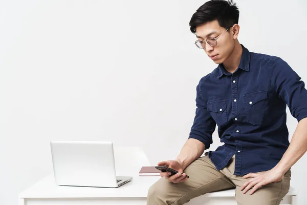 Фото молодого азиатского бизнесмена, сидящего за столом и держащего sm — стоковое фото