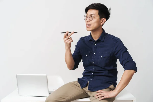 Foto de un joven hombre de negocios asiático sentado en la mesa y hablando en —  Fotos de Stock