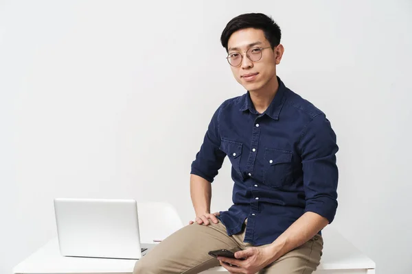 Photo of pleased asian businessman sitting at table and holding — Stock Photo, Image