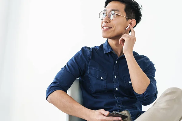 Foto de belo empresário chinês de 20 anos vestindo fones de ouvido sentado — Fotografia de Stock