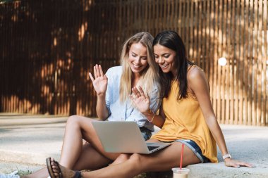 Parkta dizüstü bilgisayar kullanan iki gülümseyen genç kız