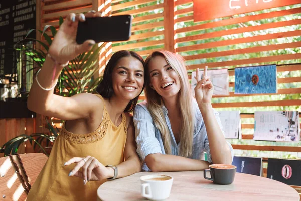 Zwei fröhliche junge Freundinnen sitzen im Café drinnen — Stockfoto