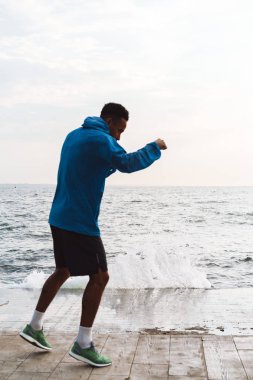 Güçlü yakışıklı genç afrikalı spor adam boksör açık plajda deniz yürüyüş boks egzersizleri yapmak.