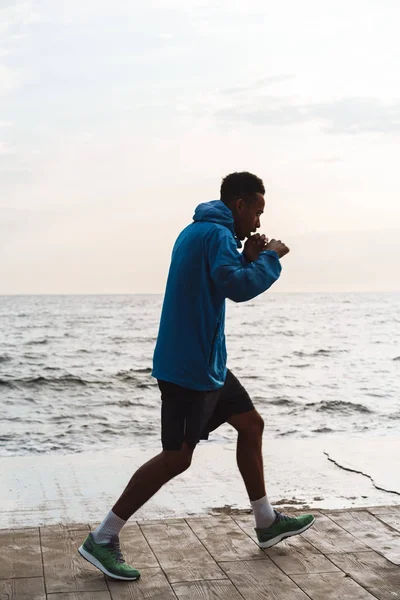 Silny przystojny młody African sportowy bokser na zewnątrz na plaży morze chodzenie zrobić boks ćwiczenia. — Zdjęcie stockowe