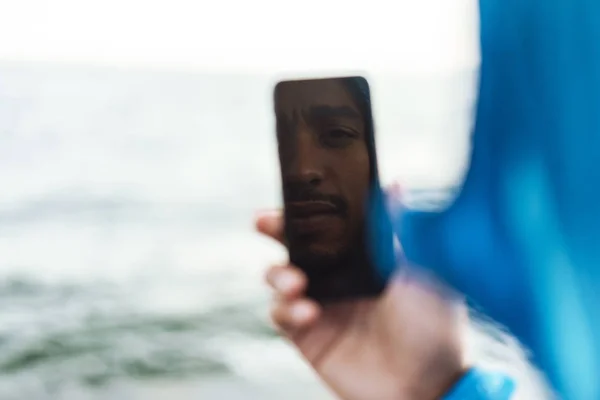 Knappe jonge Afrikaanse sportman buitenshuis op het strand zee met behulp van mobiele telefoon nemen selfie praten. — Stockfoto