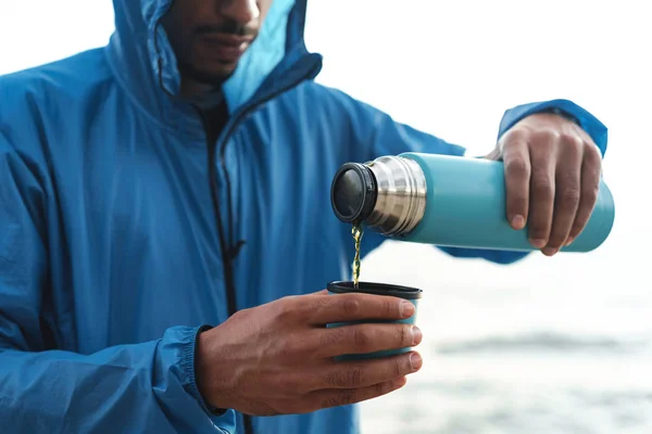 Strong handsome young african sports man outdoors at the beach sea drinking hot tea. — Stock Photo, Image