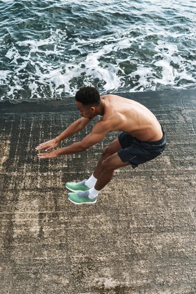 Bello giovane uomo sportivo africano all'aperto in spiaggia mare a piedi fare esercizi . — Foto Stock