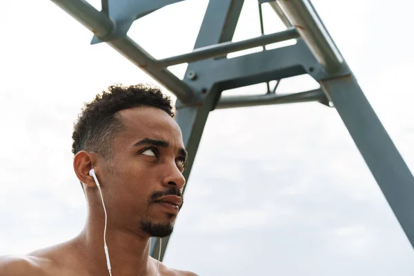 Forte bonito jovem homem de esportes africanos ao ar livre na praia mar andando fazer exercícios ouvir música com fones de ouvido . — Fotografia de Stock