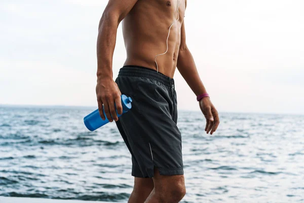Yakışıklı genç Afrikalı spor adam plaj deniz holing şişe su ile açık havada. — Stok fotoğraf