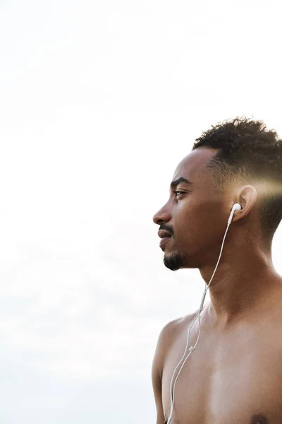 Bonito jovem homem de esportes africanos ao ar livre na praia mar ouvir música com fones de ouvido . — Fotografia de Stock