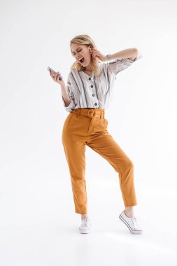 Earpod üzerinden müzik dinlerken şarkı söyleyen ve cep telefonu tutan genç kadının tam uzunlukta fotoğrafı
