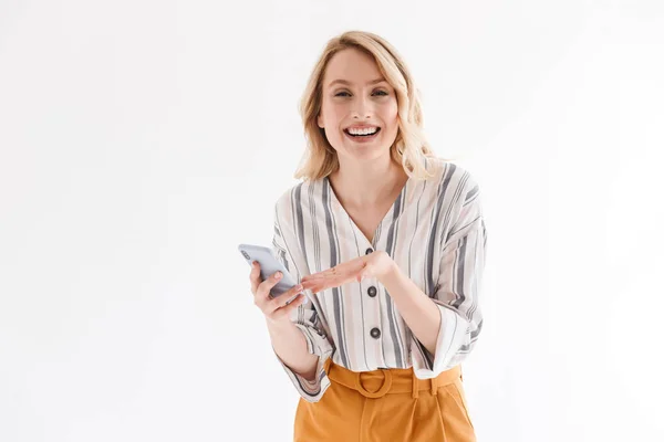 Foto de mulher loira caucasiana vestindo roupas casuais sorrindo para a câmera e apontando para o smartphone — Fotografia de Stock