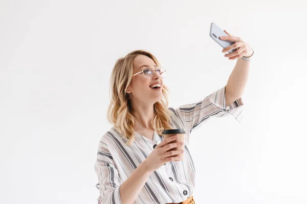 Photo d'une femme caucasienne souriante portant des lunettes prenant une photo selfie et tenant une tasse en papier — Photo