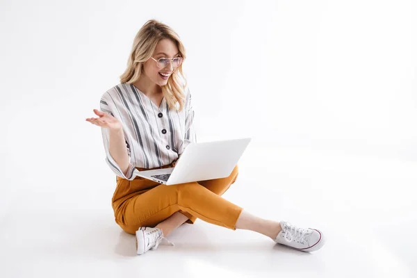 Εικόνα της όμορφης γυναίκας φορώντας γυαλιά χαμογελώντας και κοιτάζοντας το laptop ενώ κάθονται στο πάτωμα — Φωτογραφία Αρχείου