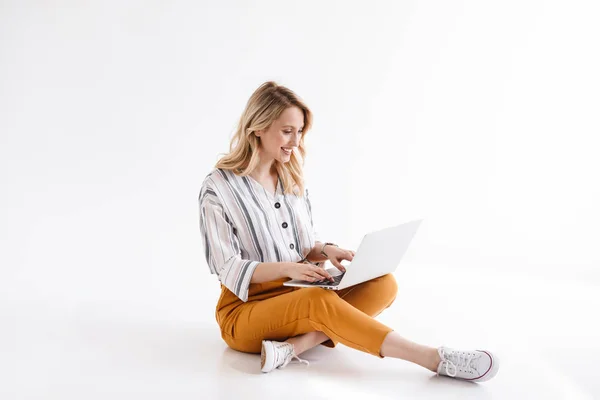 Imagem da bela mulher sorridente vestindo roupas casuais digitando no laptop e sentado no chão — Fotografia de Stock