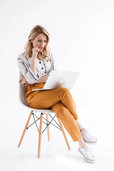 Retrato de una chica con ropa casual mirando al portátil y sentada en una silla — Foto de Stock