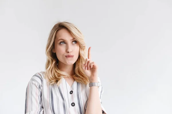 Портрет молодой блондинки в повседневной одежде, смотрящей на пространство копирования и указывающей пальцем вверх — стоковое фото