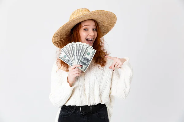 Νεαρό χαριτωμένο κορίτσι κοκκινομάλλα θέτουν απομονωμένη πάνω από λευκό φόντο τοίχο φορώντας καπέλο κρατώντας χρήματα. — Φωτογραφία Αρχείου