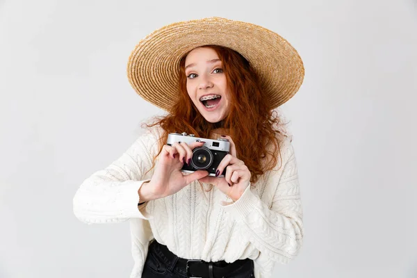 Feliz jovem bonito menina ruiva posando isolado sobre branco parede fundo usando chapéu segurando câmera . — Fotografia de Stock