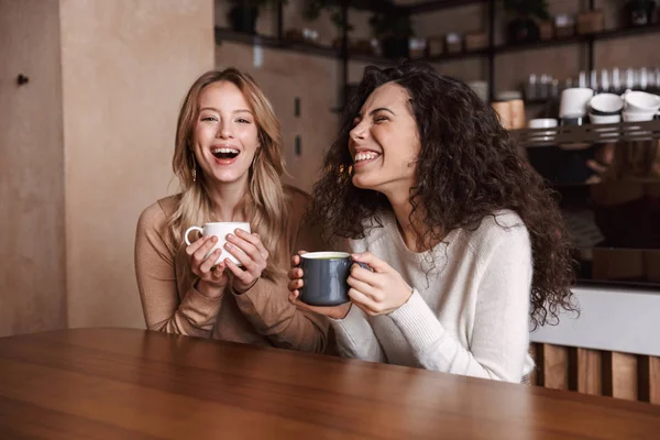 Chicas felices amigos sentados en la cafetería hablando entre sí beber té o café . —  Fotos de Stock