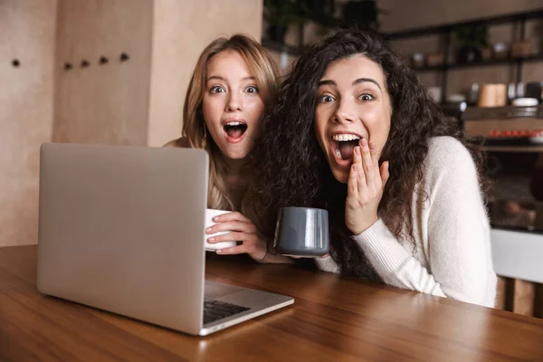 Emocional chocado meninas amigos sentados no café usando computador portátil . — Fotografia de Stock