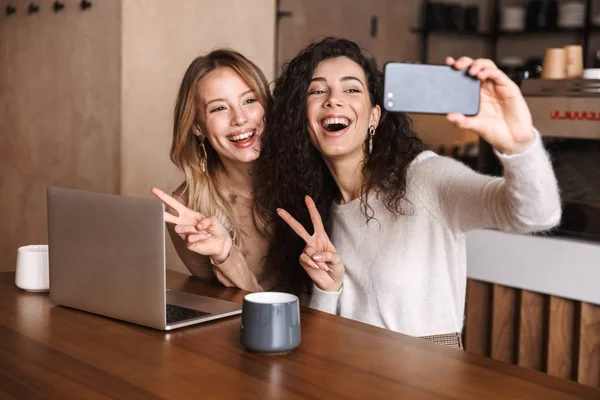 Dos alegres amigas jóvenes sentadas en la mesa del café —  Fotos de Stock