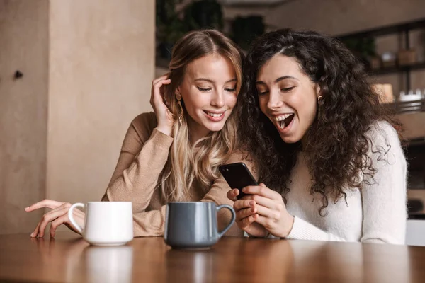 Citově šokované dívky, přátelé sedící v kavárně s mobilním telefonem. — Stock fotografie