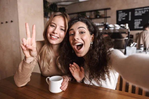 Upphetsad lyckliga vackra flickor vänner sitter i Café ta en selfie av kameran. — Stockfoto