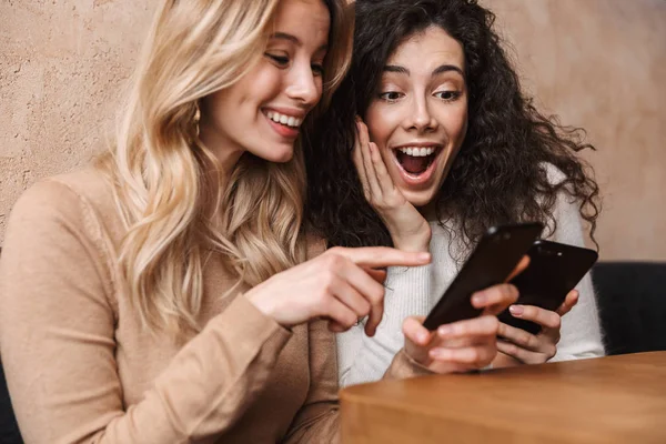 Érzelmi megdöbbent lányok barátai ülve kávézóban mobiltelefonnal. — Stock Fotó