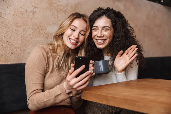 Emotioneel geschokt meisjes vrienden zittend in café met behulp van mobiele telefoon. — Stockfoto