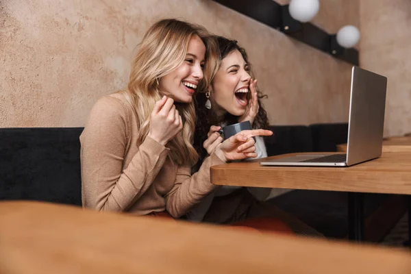 Podekscytowany szczęśliwy ładne dziewczyny przyjaciele siedzi w kawiarni za pomocą komputera przenośnego wskazując. — Zdjęcie stockowe