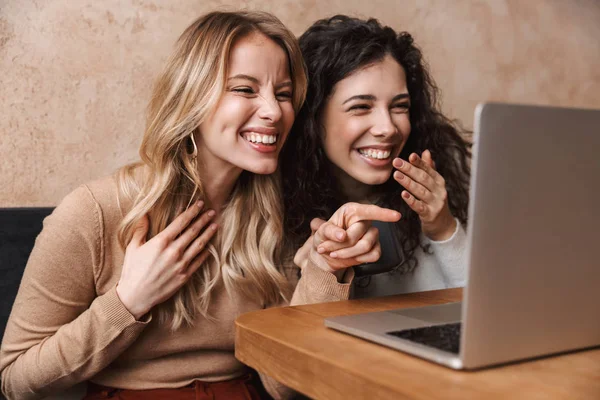 Heyecanlı mutlu güzel kız arkadaşlar laptop bilgisayar işaret kullanarak kafede oturan. — Stok fotoğraf