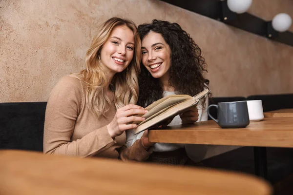 Vackra flickor vänner sitter i Café dricka kaffe läsning bok. — Stockfoto