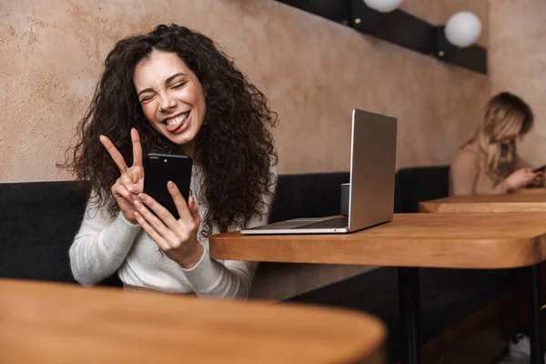 Mutlu kız dizüstü bilgisayar ve cep telefonu kullanarak kafede oturan. — Stok fotoğraf